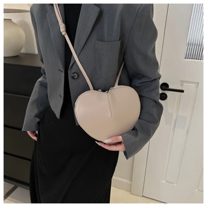 Close-up of heart-shaped cream crossbody bag with leather strap and zipper detail