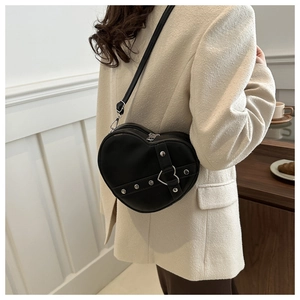 Detail of heart-shaped black crossbody bag featuring silver rivets and metal buckle