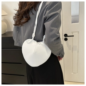Close-up of white heart-shaped crossbody bag made of smooth leather worn by a model