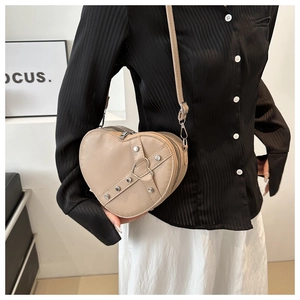Detail view of heart-shaped beige crossbody bag with metal rivets and strap on model