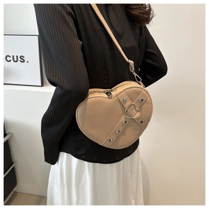 Detail showing the heart-shaped crossbody bag with metal rivets on a model shoulder