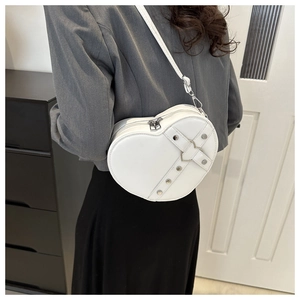 Detail of white heart-shaped crossbody bag with silver rivets and metal buckle on a model