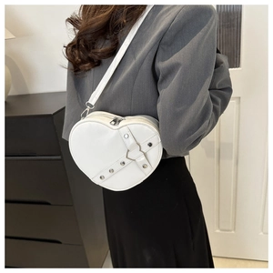 Detail of white heart-shaped crossbody bag with silver studs and metal buckle on a model