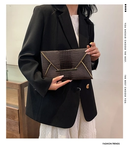 Detail of dark brown croc-textured envelope clutch with golden V-shaped metal trim