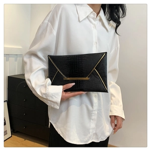 Detail of black envelope clutch featuring crocodile texture and gold metallic hardware bar