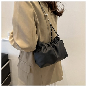 Detail of black pleated PU leather cloud bag with chain strap worn by a model