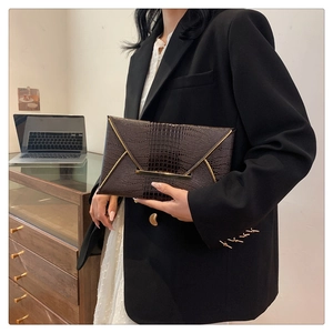 Detail of dark brown crocodile pattern envelope clutch bag with gold metal trim and flap