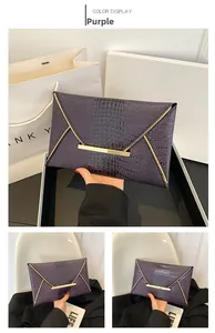 Detail of purple envelope clutch bag with crocodile texture and gold metal trim