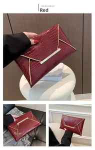 Detail of red crocodile texture envelope clutch with elegant gold metal trim closure