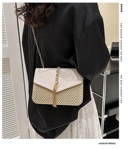 Detail of straw woven crossbody bag featuring a leather flap and gold tassel accent