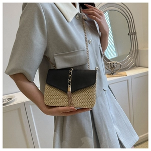 Detail of woven straw crossbody bag with black leather flap and golden tassel charm