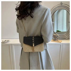 Detail of woven straw crossbody bag with black leather flap and gold chain strap