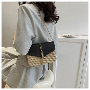 Close-up of woven straw and black leather crossbody bag with golden chain and tassel detail
