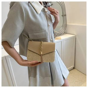 Detail of woven straw handbag featuring beige leather flap and gold tassel chain strap