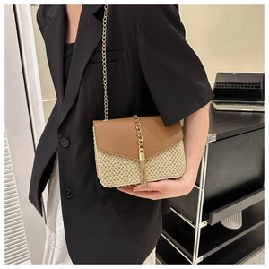 Detail of straw crossbody bag featuring a leather flap and elegant gold tassel pendant
