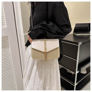 Detail of woven straw crossbody bag featuring cream faux leather flap and gold tassel