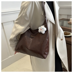 Deep brown glossy shoulder bag with a cute white cloud plush charm on a beige trench coat