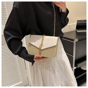Detail of woven straw crossbody bag with white leather flap and gold chain tassel