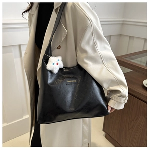 Close-up of black faux leather tote with plush cat charm and fashion brand label