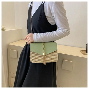 Detail of woven straw crossbody bag with green flap and gold tassel chain on model