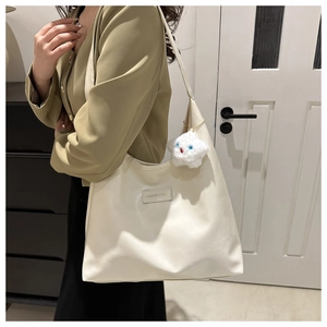 Detail view of large cream tote bag with leather logo patch and plush star charm accessory