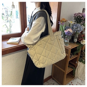 Quilted beige nylon tote bag with rhombus pattern worn on shoulder in a bright room