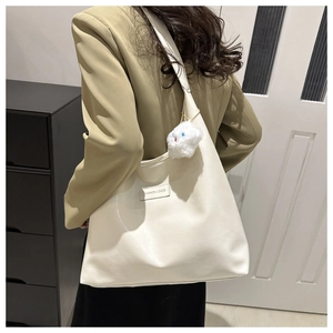 Close-up of cream faux leather tote bag featuring a plush cloud charm and embossed tag