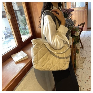 Quilted beige nylon tote bag shown on model in a sunlit vintage room setting