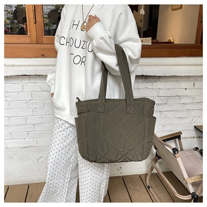 Detail of dark green quilted nylon tote bag featuring side pockets and reinforced handles