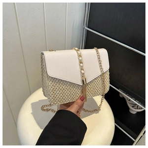 Detail of woven straw bag featuring gold chain strap and elegant metallic tassel decoration