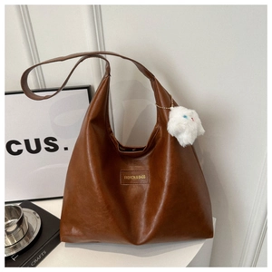 Detail of a dark brown large tote bag with retro cracked leather texture and rabbit charm