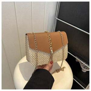 Detail of woven straw crossbody bag with leather flap, metal chain and decorative tassel