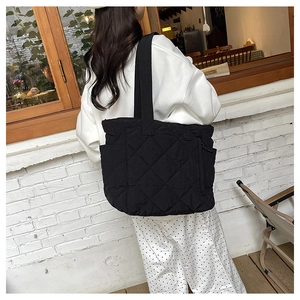 Detail of black quilted nylon tote bag with large diamond patterns and side pockets