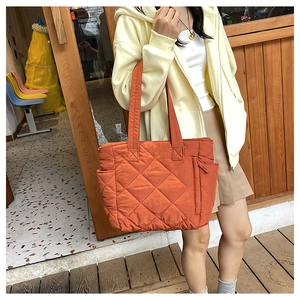 Detail of orange quilted nylon tote bag featuring diamond lattice stitching and side pocket