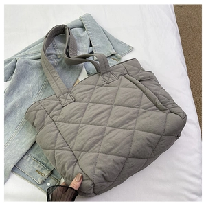 Detail of grey quilted nylon puffer tote bag featuring diamond pattern on denim background