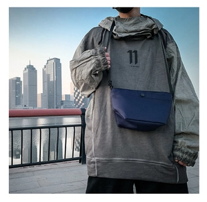 Detalle del bolso bandolera de nailon azul marino con una sudadera gris con capucha