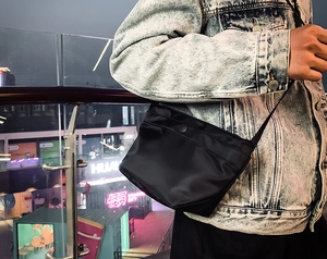 Primer plano de un bolso bandolera de nailon negro con botón a presión en una chaqueta