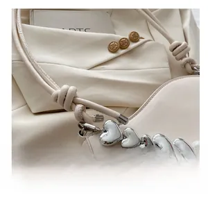 Gros plan du sac en cuir beige avec nœud décoratif et chaîne argentée en forme de cœur