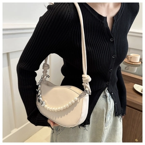 Détail du sac selle crème avec chaîne de perles élégante et pendentif en cœur