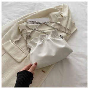 Close-up of white ruched cloud bag with silver chain on a beige blazer, minimalist style