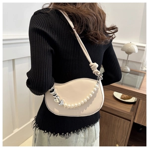 Détail du sac selle crème avec chaîne en perles, pendentif cœur et design ondulé chic
