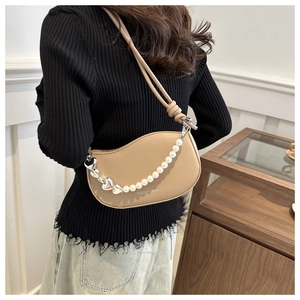 Détail du sac selle beige orné d'une chaîne en perles et d'un pendentif en cœur