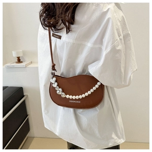 Détail d'un sac demi-lune marron avec chaîne en perles et breloque cœur sur un mannequin