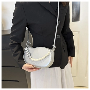 Détail du sac demi-lune argenté avec chaîne en perles et breloques en cœur sur la bandoulière