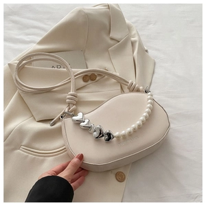 Détail du sac selle blanc cassé avec chaîne perle cœur sur fond de blazer élégant