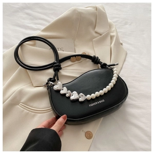 Détail du sac selle noir avec chaîne à cœurs en métal et perles sur blazer crème