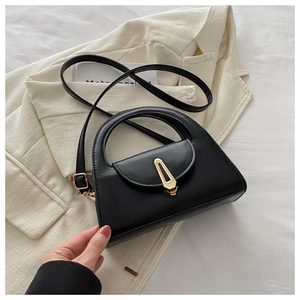 Detail einer schwarzen Trapez-Handtasche mit Cut-out-Griff und goldenem Metallschloss