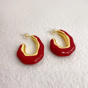Modern red enamel C-shaped earrings with gold metal edges in a 45-degree studio view