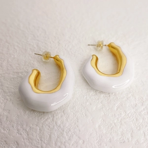 Irregular C-shaped earrings with white enamel finish and gold lining on white background