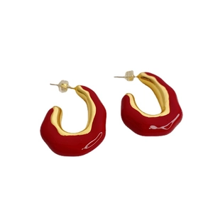 Modern golden C-shaped hoop earrings with red enamel glaze on a white background